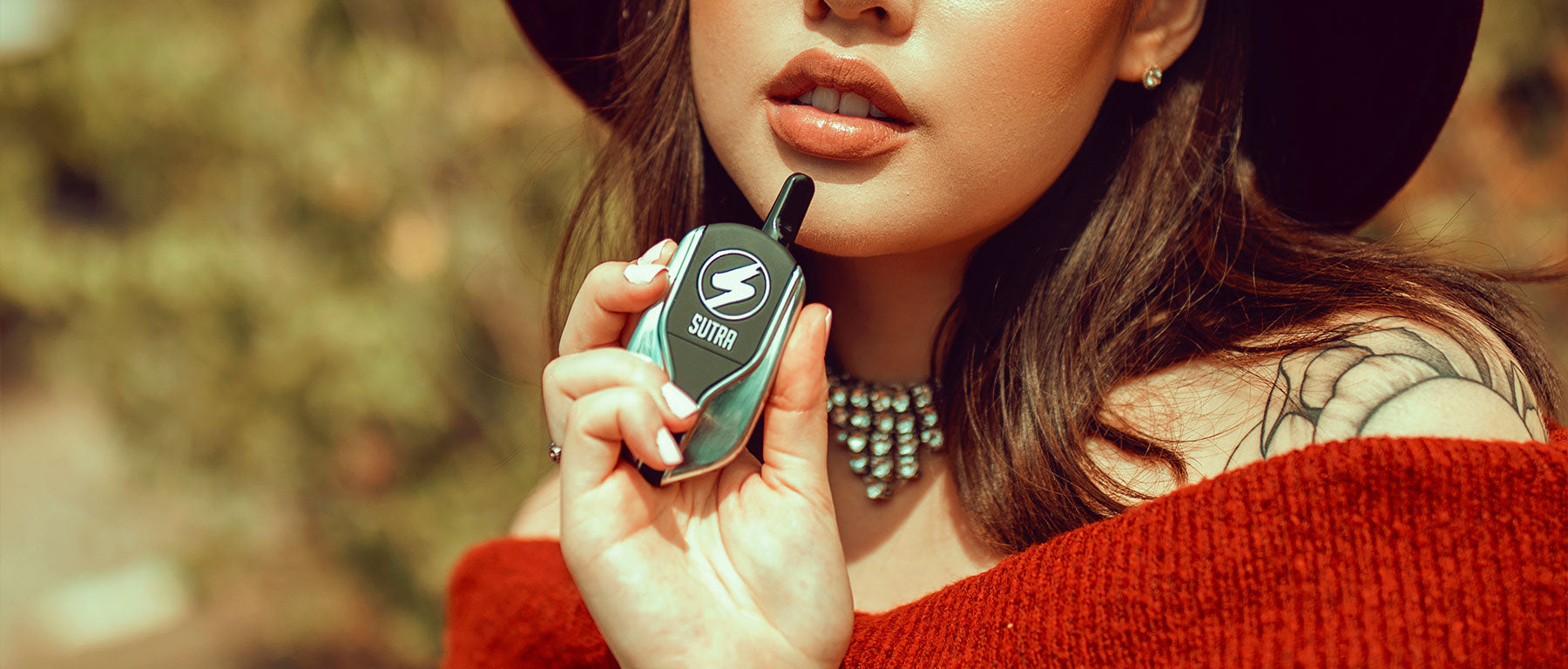 Woman in red sweater holding silver Sutra Squeeze outside at park