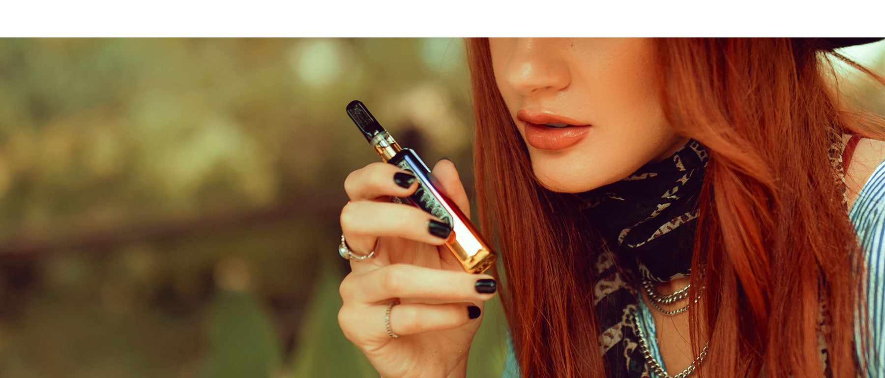 Woman with red hair holding Portable Vaporizer Sutra Stik outside near park
