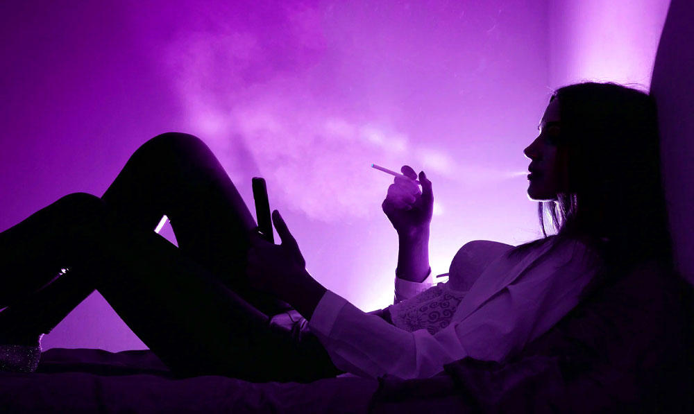 Woman relaxing with a vape under soft purple studio lighting