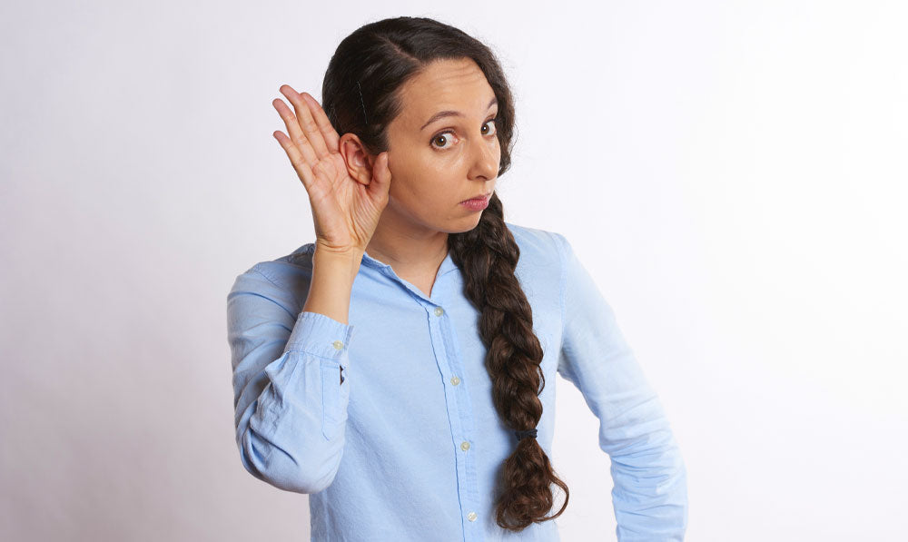 Woman listening for a sound in front of a white wall