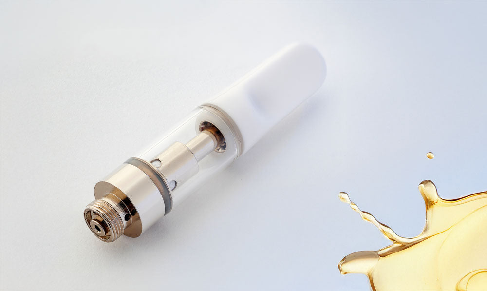 Empty oil cartridge resting on white surface with golden oil spill nearby
