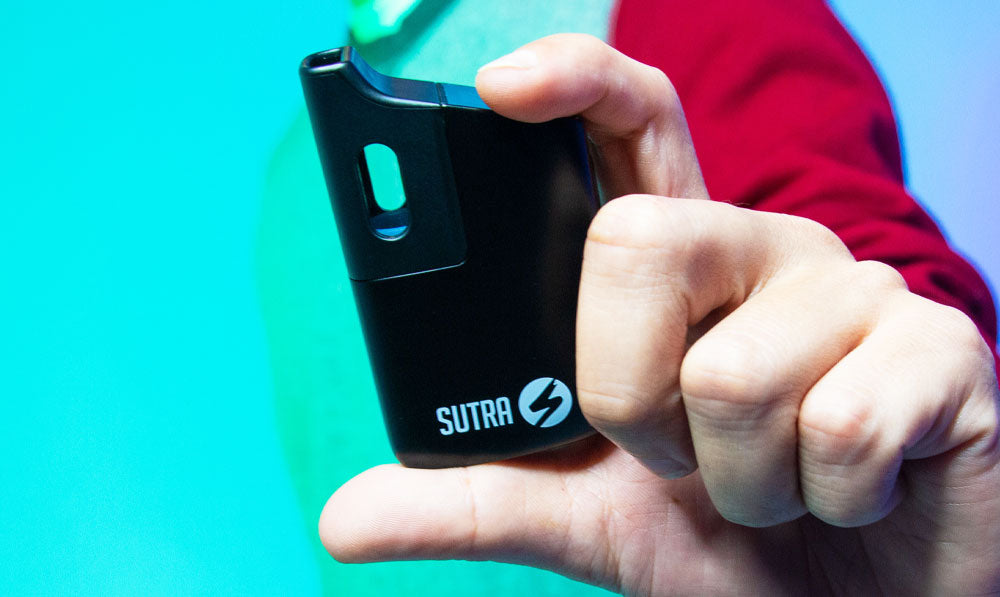 Man in a sweater holding Sutra Mini against teal studio background