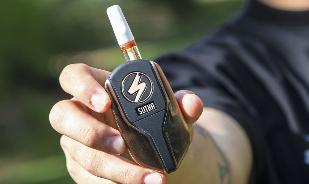 Person holding a bronze Sutra Squeeze vaporizer on a park trail