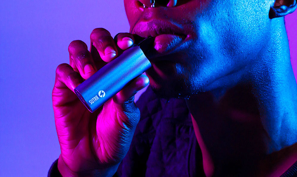 Person holding a purple Sutra Auto vaporizer under purple lighting