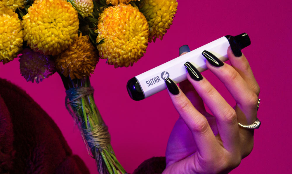 Woman holding Sutra Mini in front of pink studio background with flower display