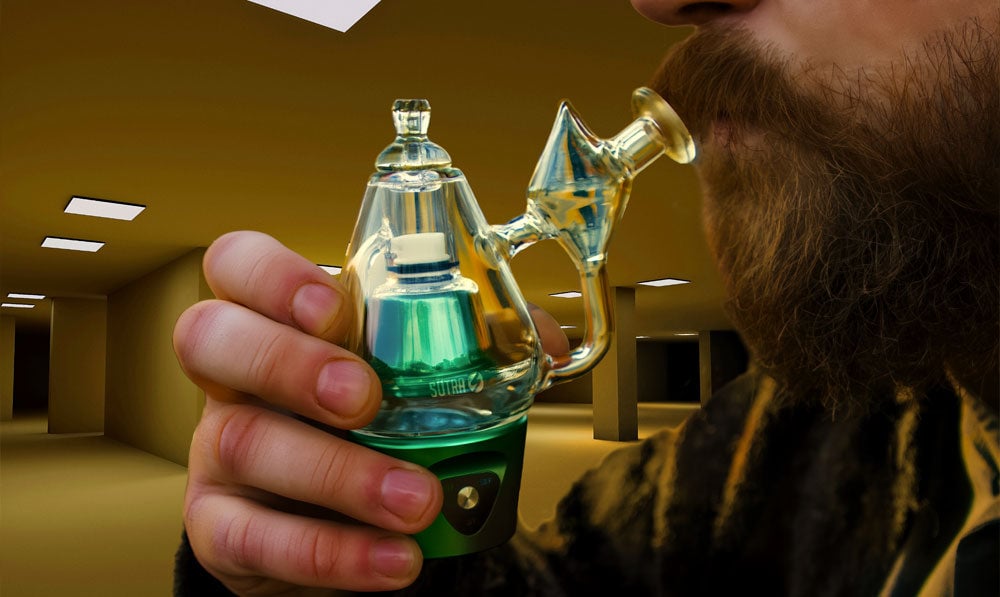 Man with beard in backrooms style atmosphere taking a hit of the Sutra Vape DBR Pro Portable Concentrate Vaporizer in greenish color